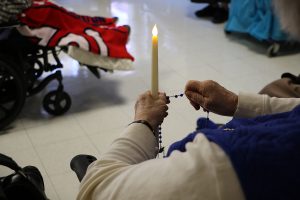 hands holding a candle and rosary beads